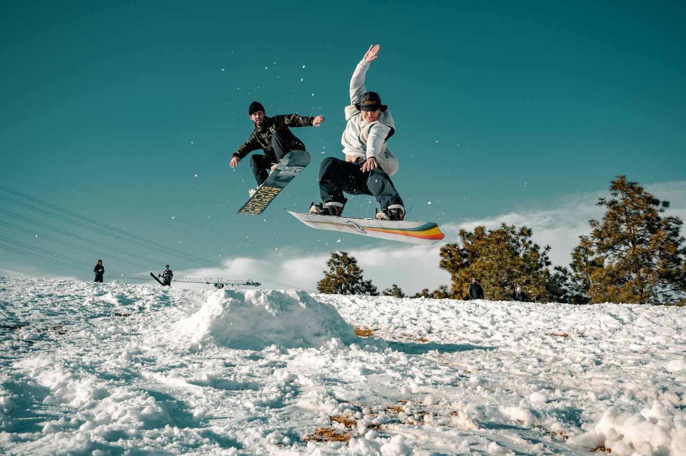 Twee snowboarders springen samen over de kicker